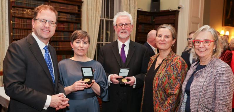 Five people standing in a room, two with gold medals